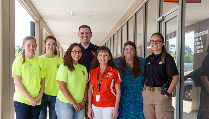 row of 7 parking staff members from SHSU smiling outside their parking office
